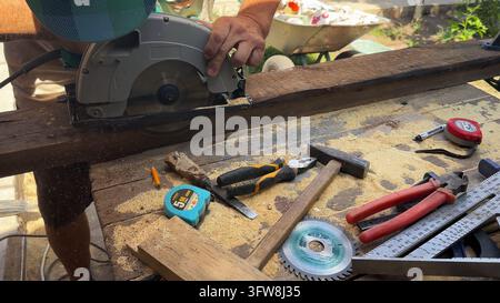 Arms of professional repairman sawing wooden construction with a circular saw at construction. Male hands of adult craftsman cuts wood using electric Stock Photo