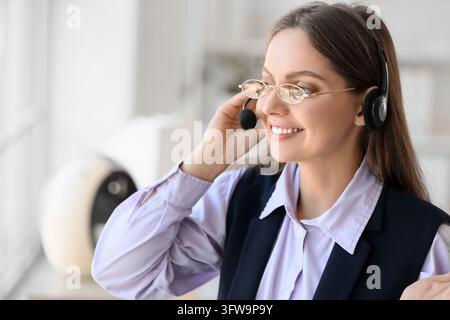 Customer support and remote assistance, smiling woman with headset and glasses working in office environment for professional communication services Stock Photo
