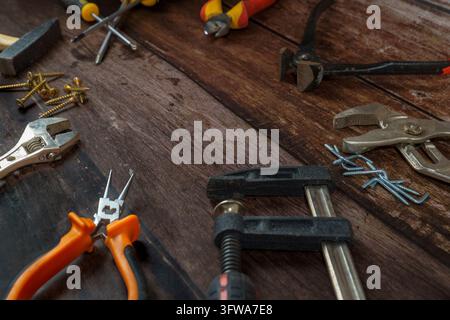Various diy and carpentry tools including wrench, pliers, hammer, screwdrivers, clamp, screws, and nails on a wooden background Stock Photo