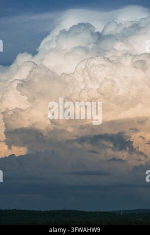 Towering cumulonimbus clouds dominate the sky, illuminated by the warm hues of the setting sun, creating a dramatic and awe-inspiring scene above a tranquil forest landscape Stock Photo