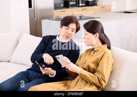 Couple Having A Serious Discussion On The Living Room Couch While Looking At Their Phones Stock Photo