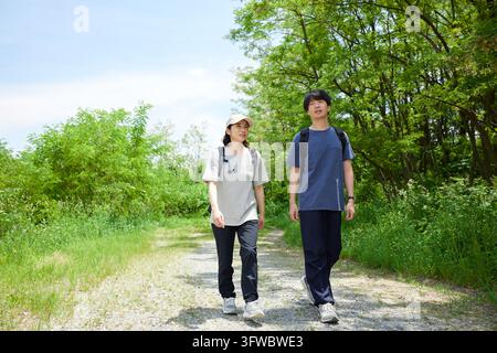 Man And Woman Hiking Along A Mountain Trail Lined With Fresh Greenery Stock Photo