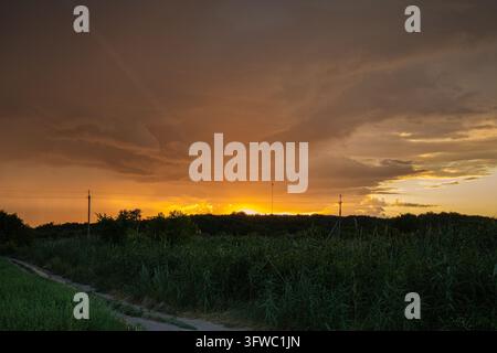 Dramatic Orange Sunset Beneath Dark Clouds Over a Rural Landscape Stock Photo