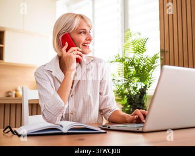 Successful remote professional smiling during a phone conversation while working from home. Stock Photo