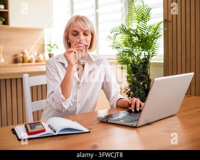 Blond woman working from home, she is drinking water. Stock Photo