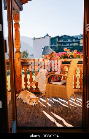 Woman sits on balcony with dog, morning light in outdoor setting Stock Photo