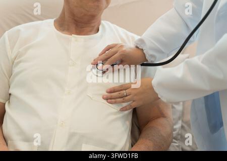 Nurse using stethoscope to check heartbeat of a senior patient in hospital bed for health assessment. Ideal for healthcare, wellness, and patient care Stock Photo