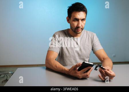 Concept of do it yourself electronics repair and maintenance. Man focused on fixing broken gadget at home. Studio shot with blue gradient background a Stock Photo