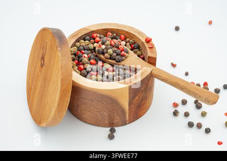Round wooden spice container filled with mixed peppercorns and wooden spoon on white background, rustic closeup image of seasoning Stock Photo
