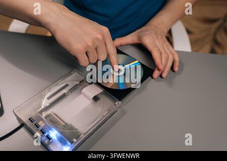 Top view of person interacting with computing hardware, loading data storage disc into portable optical drive, connecting to personal computer for Stock Photo