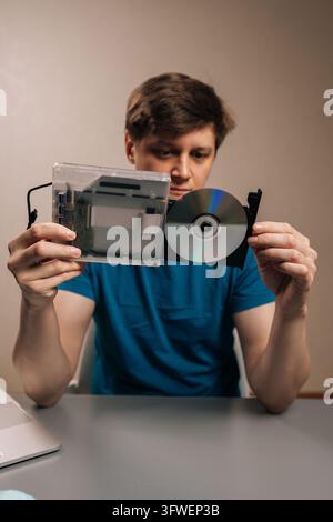 Vertical portrait of man holding and presenting external optical disc drive with transparent casing, revealing internal components alongside loaded Stock Photo