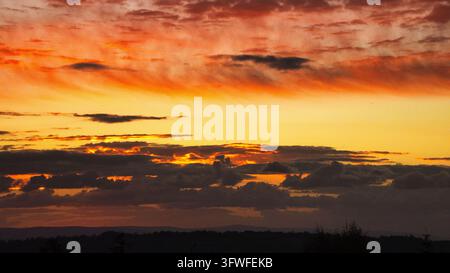 Orange yellow and red sky with dark clouds. A dark land silhouette is visible at the bottom. Stock Photo