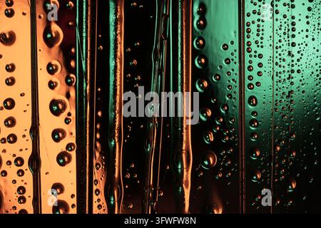Water droplets and vertical liquid streaks covering glass, glowing in contrasting orange and teal light Stock Photo
