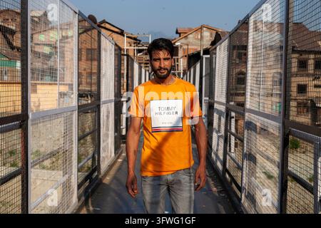 Young man in an orange t shirt standing on a fenced footbridge, Jammu and Kashmir, Srinagar, India Stock Photo