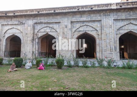 Three women sitting on the lawn in front of the arched facade of Pathar mosque, Jammu and Kashmir, Srinagar, India Stock Photo