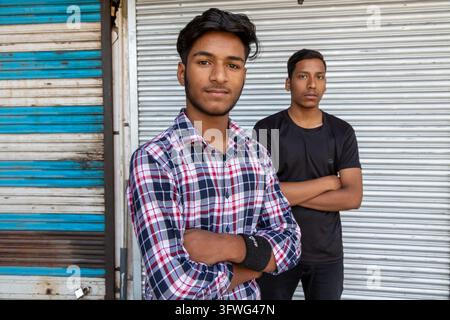 Two young men with crossed arms standing in front of a metal shutter, Jammu and Kashmir, Srinagar, India Stock Photo