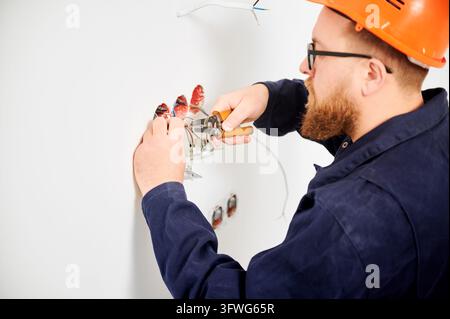 Electrician stripping wires with tool and preparing connections in wall sockets. Close up of electrical installation process, cable work and home renovation concept Stock Photo