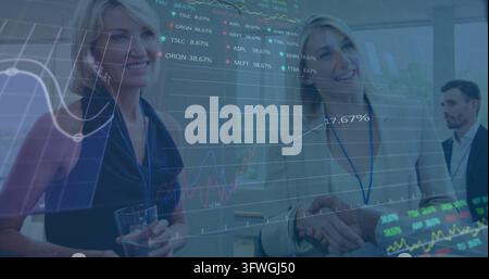 Shaking two women in business attire exchanging handshake in conference with lanyards and charts Stock Photo