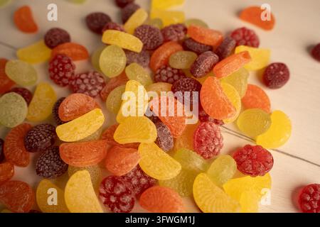 close-up photo of a scattered pile of colorful sugar-coated gummy candies on a light wood tabletop, showing yellow, orange, red, green and purple citr Stock Photo