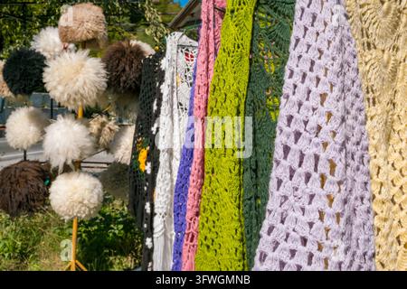 Colorful handmade knitted and crocheted textiles hanging outdoors beside fluffy woolen hats and pompom decorations at a Georgian craft displa Stock Photo