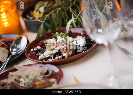 A close-up view of a roasted vegetable dish topped with crumbled cheese and pomegranate seeds served on a rustic plate. Stock Photo