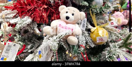 Cute teddy bear ornament with festive details displayed among Christmas decorations in an airport shop creates a warm holiday gift mood. Stock Photo