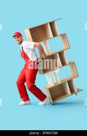 Moving service and furniture delivery, professional mover in red uniform carrying wooden shelving unit on blue background Stock Photo