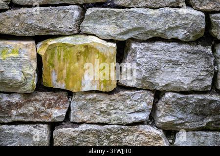 A close view shows weathered stone blocks stacked in courses, with rough surfaces, chipped edges, patches of discoloration and dark gaps between them. Stock Photo