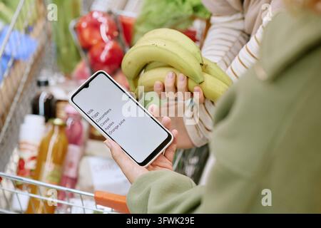 Woman Holding Smartphone with Grocery List in Supermarket Stock Photo