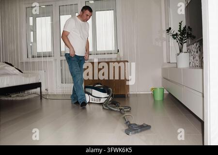 He cares about his surroundings. A happy, smiling man, dressed entirely in white, is vacuuming the room he is tidying up the house and doing some clea Stock Photo