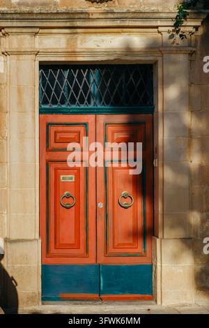 Terracotta Red and Teal Blue Wooden Front Door set in Ornamental Limestone Architrave with Diamond Metal Transom Grille Stock Photo
