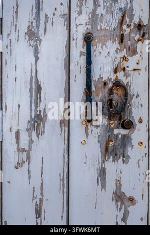 Rusting Iron Handle on Peeling White Painted Antique Wooden Door Surface with Distressed Peeling Paint Texture Stock Photo