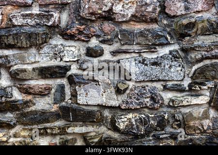 Close up of an old rustic stone wall made of irregular weathered rocks joined with mortar, rough masonry texture featuring dark gray brown and white Stock Photo