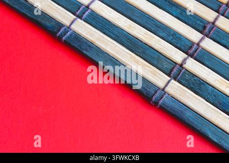 Close-up of a bamboo sushi mat placed on a vibrant red background showing natural wood grain, woven string ties and textured pattern. Stock Photo