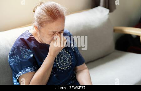 Elderly Asian woman crying wipes tears with hands feels unhappy, bad news. Stock Photo