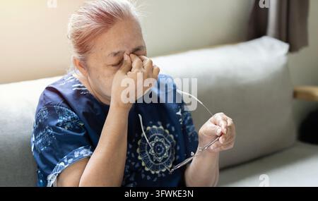 Middle-aged Asian woman taking off glasses closed eyes rubbing eyelid suffers from eye strain deterioration eyesight with age concept Stock Photo