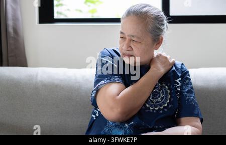 People, healthcare and problem concept - Mature attractive Asian woman suffering from pain in shoulder in the living room. Stock Photo