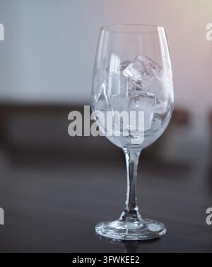 Ice cubes in an empty glass wine on a wooden bar counter, soft light background, front view with details Stock Photo