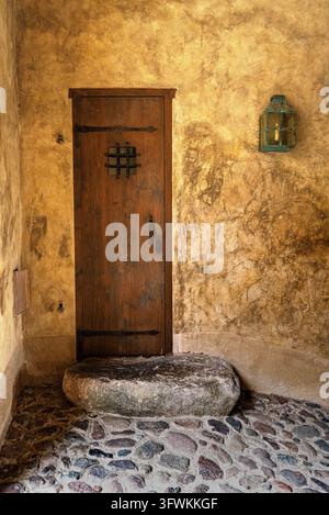 Weathered wooden door with an iron grille, decorative wall lantern and large stone step in an ochre plastered wall at Bauska Castle, Latvia. Stock Photo