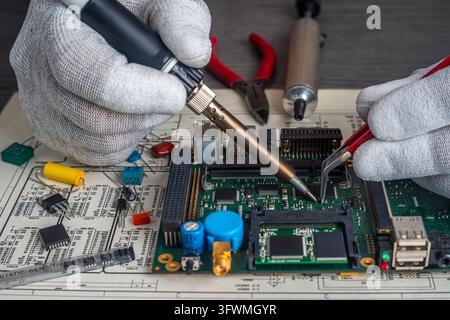 Two technicians work on a circuit board using tools for assembly and quality control in a manufacturing facility. Stock Photo