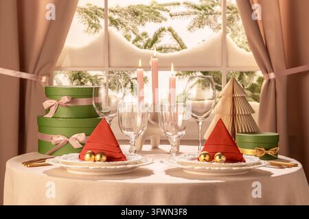 Horizontal dining table setup for two featuring red tree napkins, golden ornaments, paper christmas tree, lit candles, and stacked green gift boxes wi Stock Photo