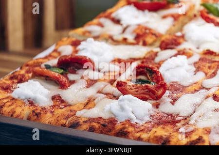 Delicious freshly baked Italian pizza topped with melted mozzarella, creamy burrata, roasted tomatoes and fresh basil leaves, close-up. Stock Photo