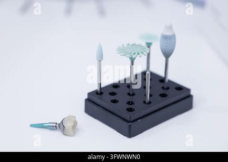 Dental burs arranged in a holder beside a tooth crown for prosthetic restoration, laboratory milling, polishing, and precision dentistry applications. Stock Photo
