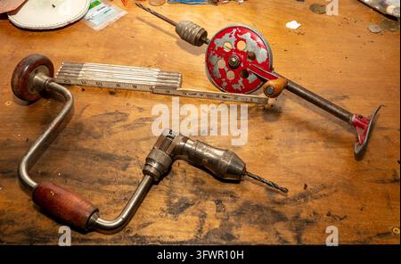 Vintage hand drills rest on a worn wooden table. Metal and wood show signs of heavy use. Tools display charm, history, and craftsmanship. Their design Stock Photo