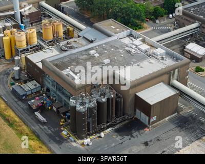 Large industrial brewery facility seen from above during the day showing outdoor metal storage tanks connected by extensive piping systems across the Stock Photo