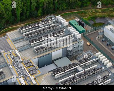 Large industrial data center building with numerous air conditioning units and cooling fans installed on the roof to maintain temperature control for Stock Photo