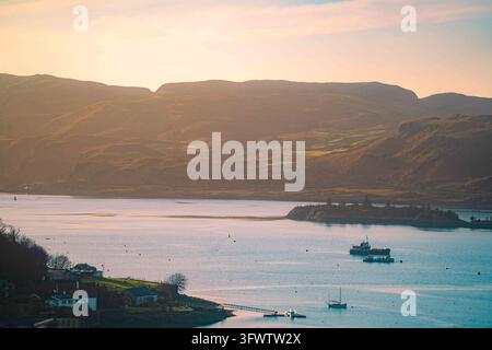 View of Oban bay at sunset with boats anchored in the calm water, surrounded by rolling hills and coastal landscape in Oban, Scotland, United Kingdom. Stock Photo
