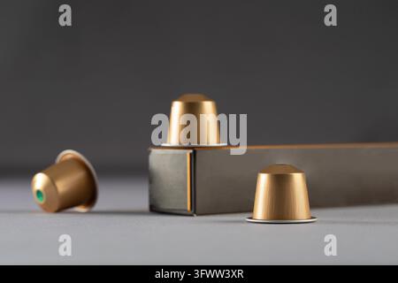 Gold coffee capsules arranged near a box on a gradient background, highlighting their sleek design and modern packaging. Perfect for coffee lovers and advertising. Stock Photo