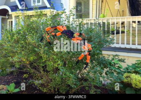 A large orange and black Halloween spider decoration rests in leafy shrubs beside a house porch with white railings in Evanston, Illinois. Stock Photo