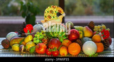 A wide horizontal eye-level shot of a festive Christmas fruit display on a wooden table, featuring a small green striped watermelon in a sparkling yel Stock Photo